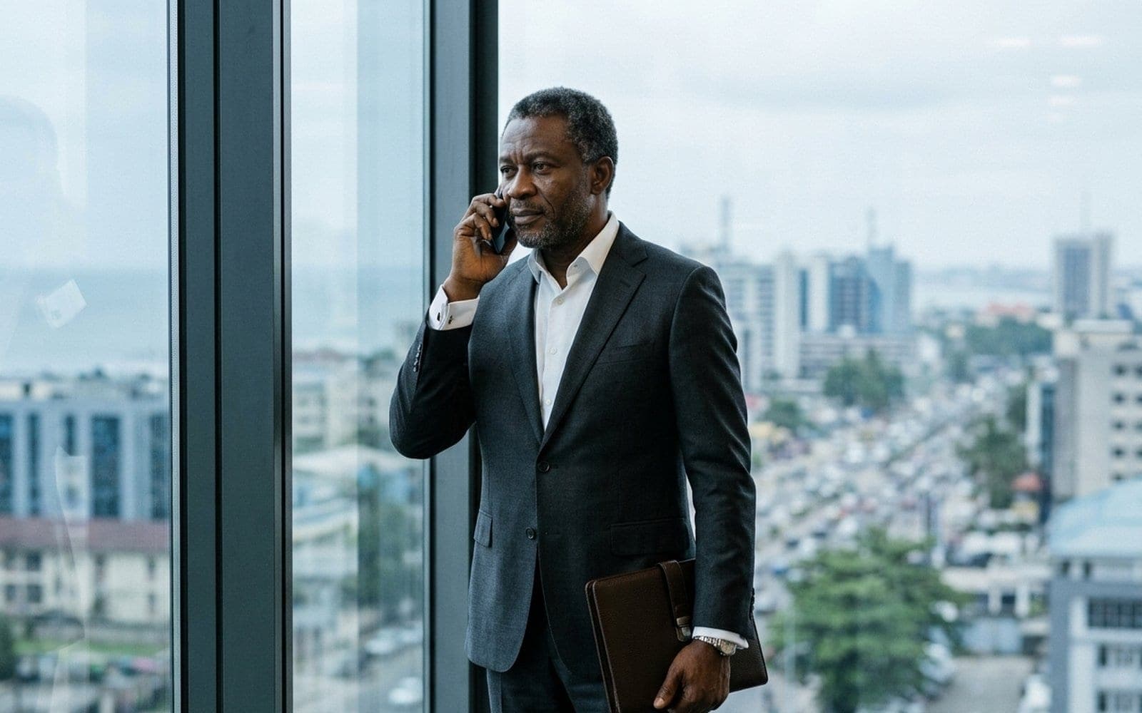 A businessman on a phone call by an office window, listening carefully.